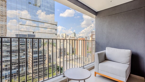 A balcony with a grey sofa and a small round table, overlooking a cityscape with modern buildings.