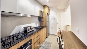 A modern kitchen with a gas stove, microwave, and wooden cabinets. - Functional Apartment in Itaim Bibi SP - Sat0012 (São Paulo)
