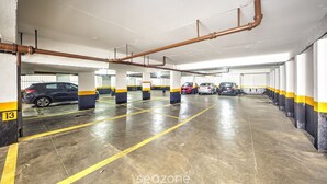 A multi-level parking garage with clear yellow lines marking parking spaces, concrete pillars, and visible cars parked inside. - Functional Apartment in Itaim Bibi SP - Sat0012 (São Paulo)