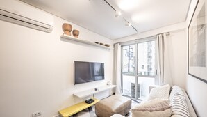 A modern living room with a flat-screen TV, a sofa, a coffee table, and a window with a city view. - Functional Apartment in Itaim Bibi SP - Sat0012 (São Paulo)
