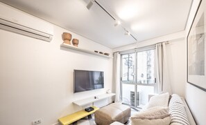A modern living room with a flat-screen TV, a sofa, a coffee table, and a window with a city view. - Functional Apartment in Itaim Bibi SP - Sat0012 (São Paulo)