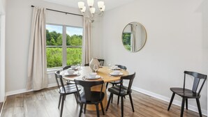 A dining room with a round table set for four, surrounded by black chairs. A chandelier hangs from the ceiling, and a round mirror is on the wall.