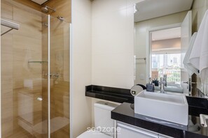 Ein modernes Badezimmer mit Duschkabine aus Glas, einem weißen Waschbecken und einer schwarzen Arbeitsplatte.