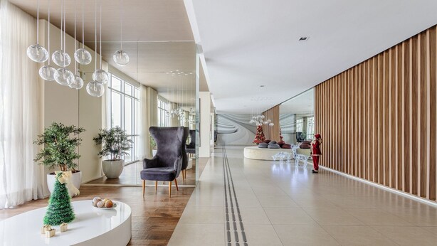 Een ruime hal met modern interieur, waaronder een grijze fauteuil, een kleine kerstboom en een wit receptiebalie.