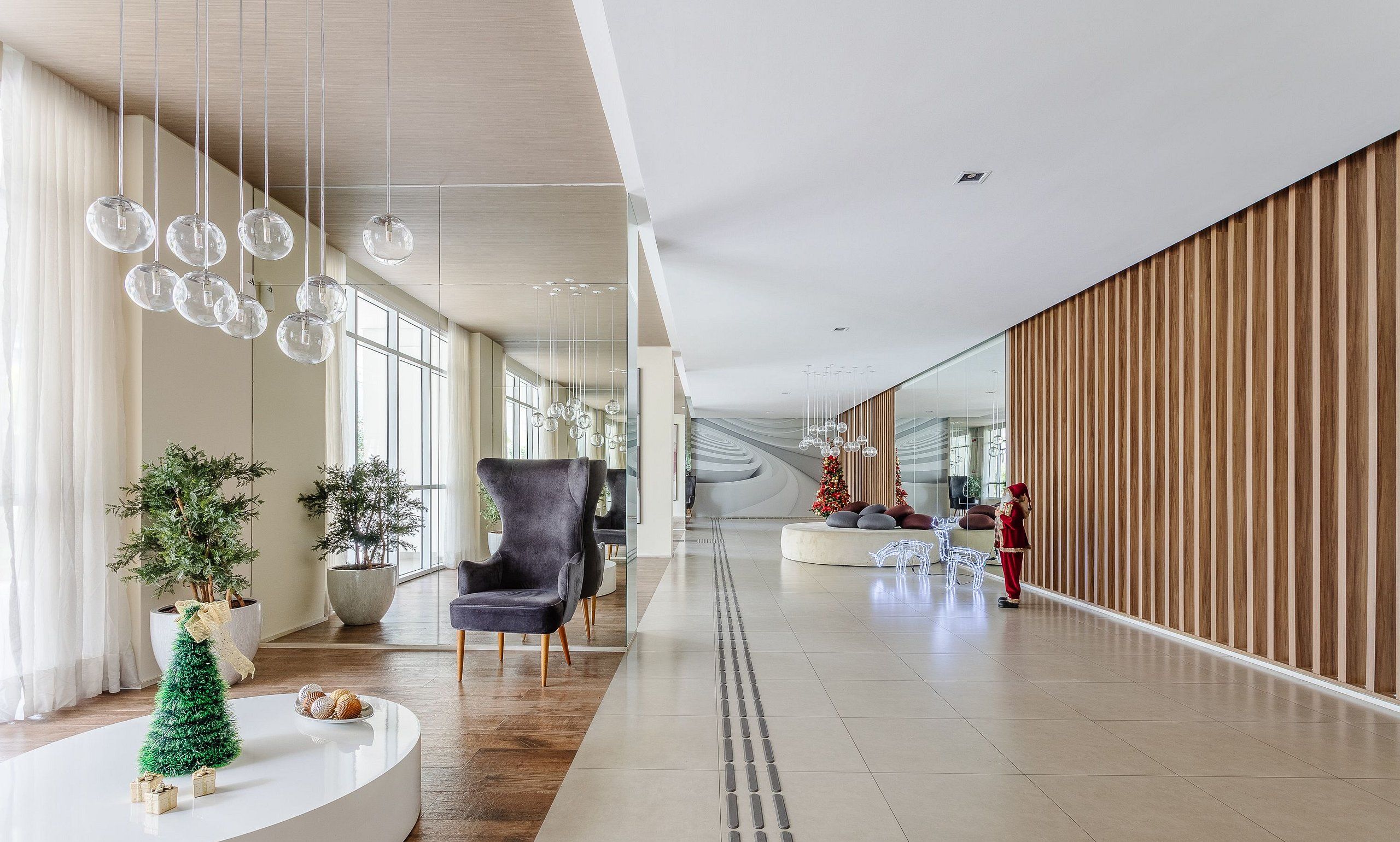 A spacious hallway with modern decor, including a grey armchair, a small Christmas tree, and a white reception desk.
