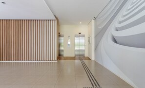 Un intérieur moderne avec un long couloir, deux ascenseurs et un mur orné de motifs.