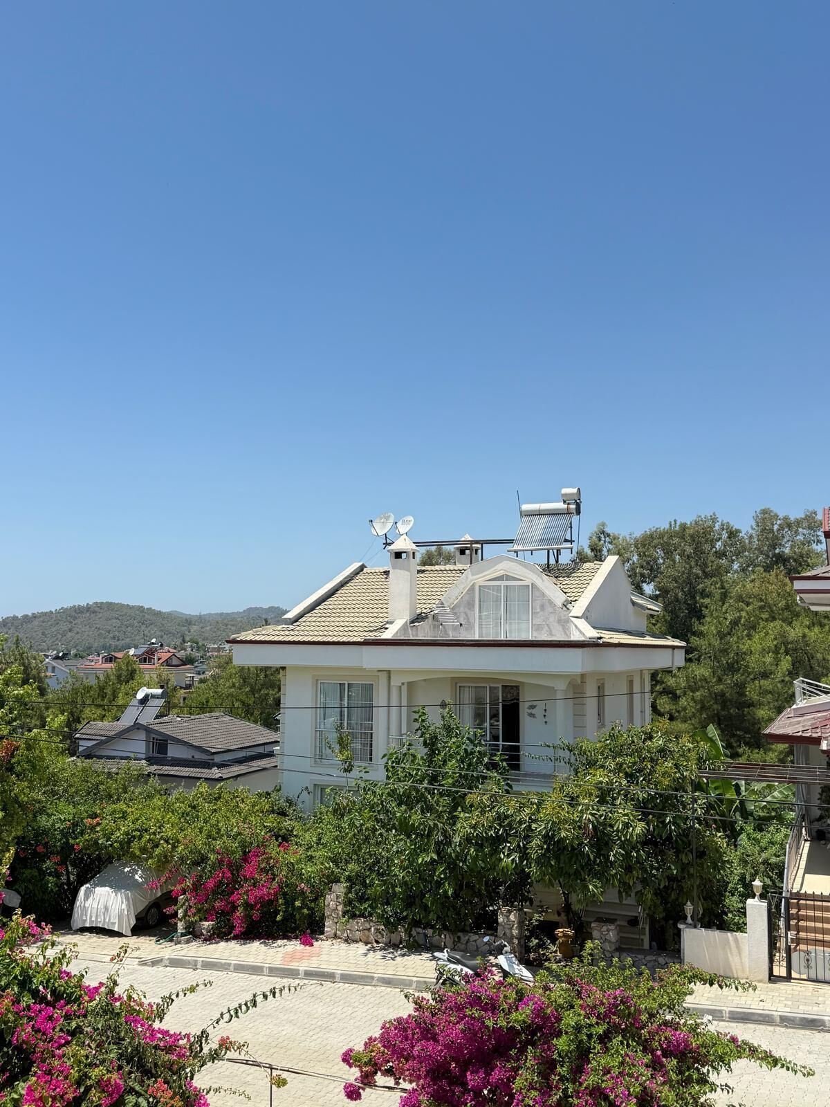 A house with a sloped roof, satellite dishes, and a garden with flowering plants.