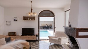 A living room with a TV, sofa, fireplace, and a view of a pool and dining area. - Luxurious home in Porec (Porec)