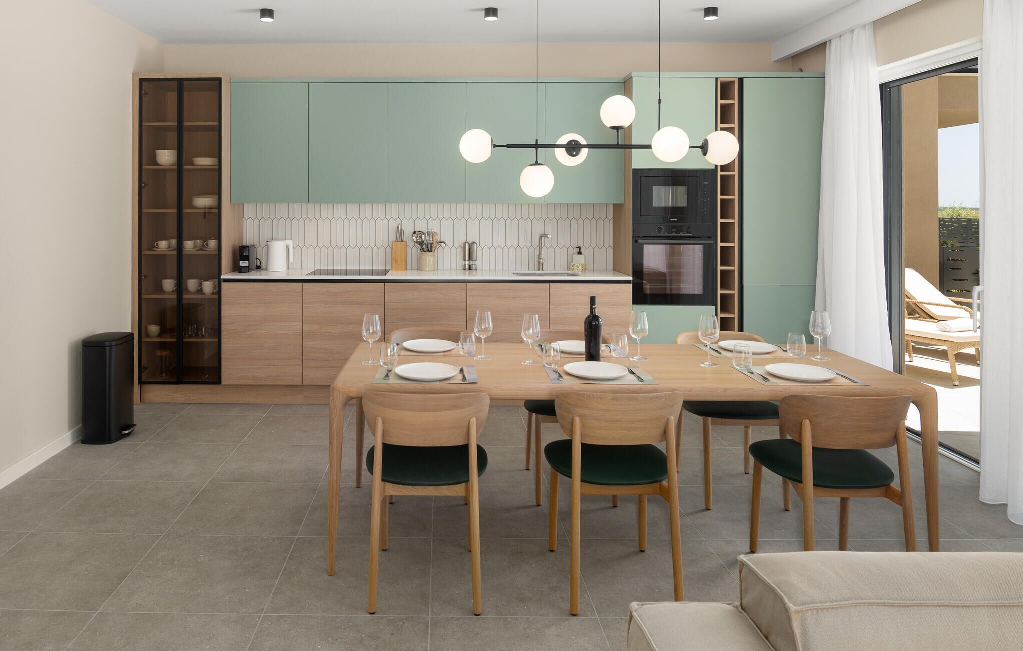 A modern kitchen with teal cabinets, a dining table set for six, and a view to a balcony.