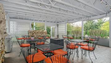 Un patio al aire libre con mesas y sillas de metal, una parrilla y una pila de leña.