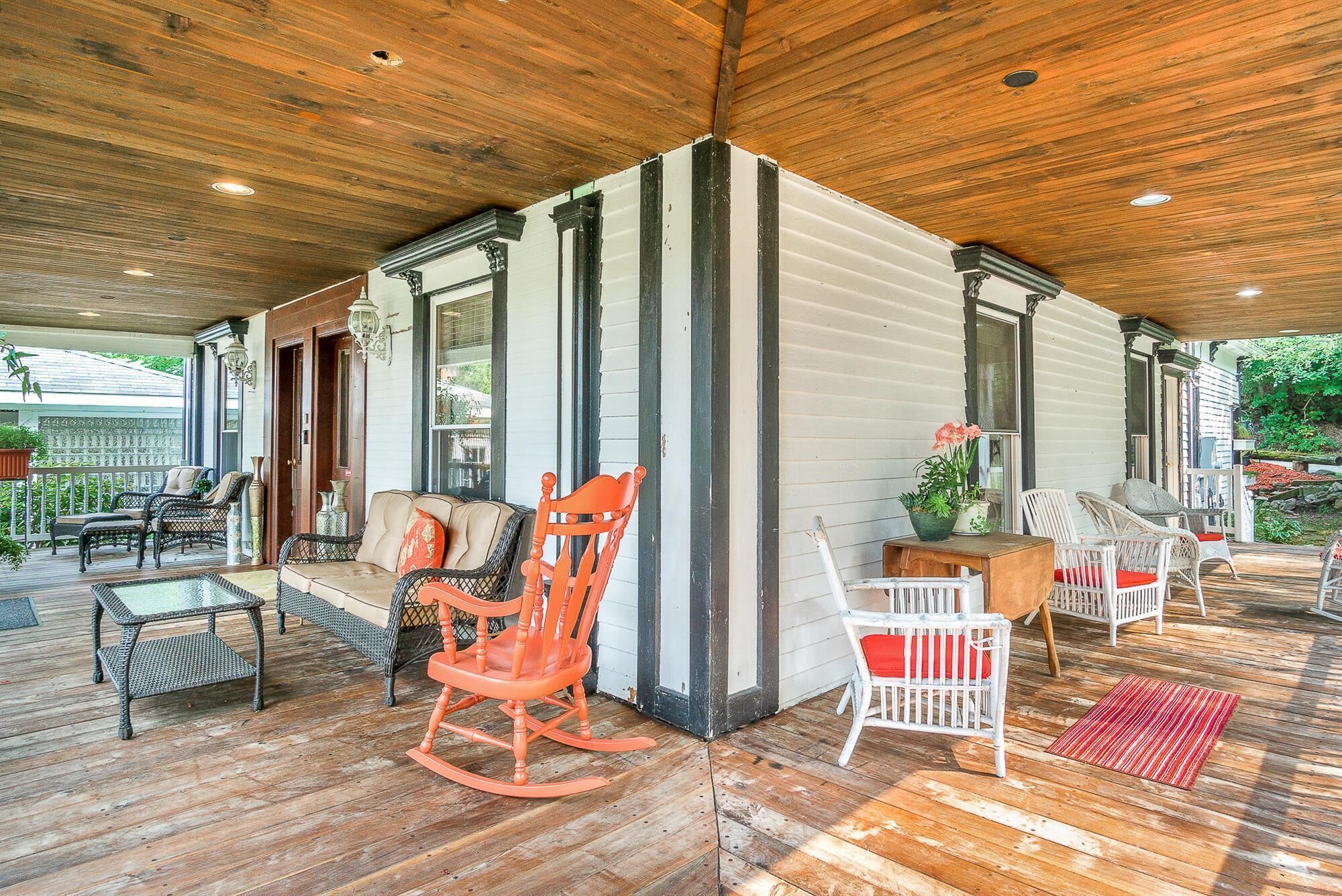 A covered porch with wicker furniture, a rocking chair, and a small table with a potted plant.