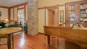 Un amplio salón con un piano de madera, una chimenea y una estantería llena de libros.