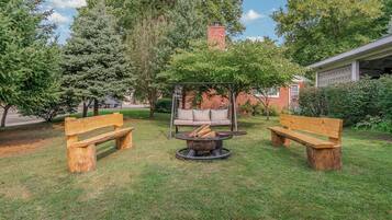 Un patio trasero con dos bancos de madera, un parque infantil y una chimenea.