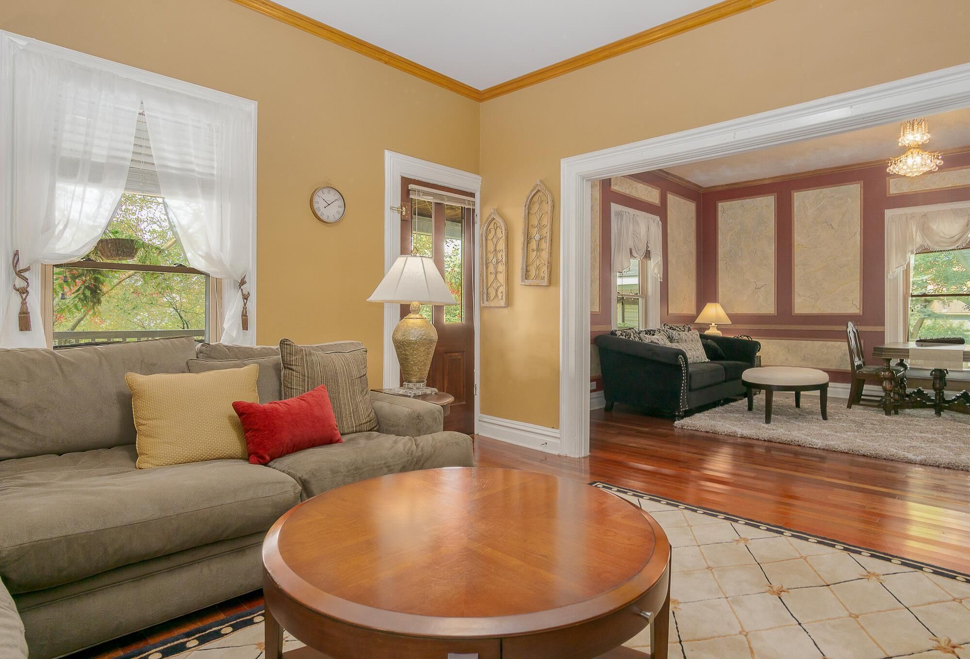 A living room with a sofa, a round coffee table, and a lamp. There is a door leading to another room.