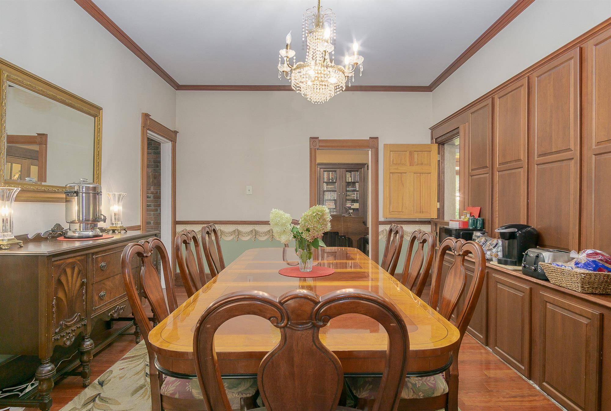 A dining room with a large wooden table, chairs, a chandelier, and wooden cabinets.