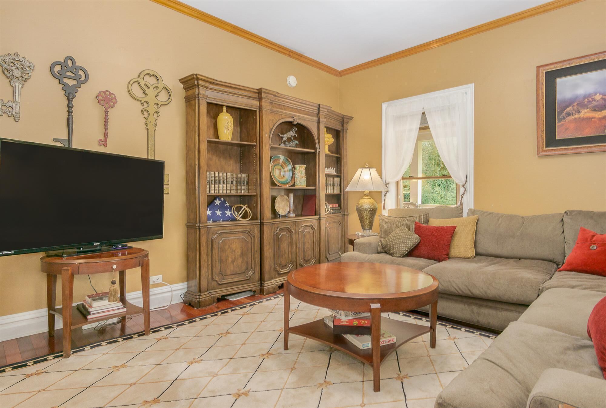 A living room with a television, a wooden cabinet, a sofa, and a window with curtains.