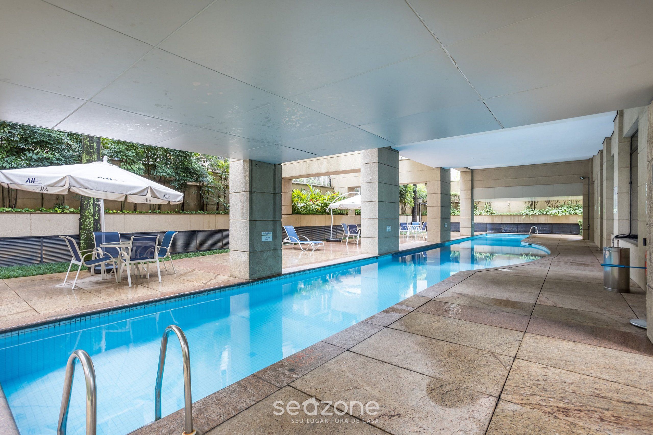 Piscina interna com água cristalina, rodeada por espreguiçadeiras e guarda-sóis, e piso revestido de azulejos.