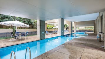 Piscina interna com água cristalina, rodeada por espreguiçadeiras e guarda-sóis, e piso revestido de azulejos.
