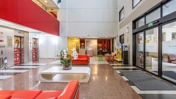 Um lobby moderno com assentos vermelhos, um balcão de recepção branco e uma fachada de vidro.