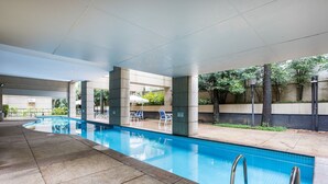 A swimming pool with clear blue water, surrounded by lounge chairs and umbrellas, with a concrete floor and a low wall with greenery. - Modern Studio Just 300m From Moema Metro Sqc0810 (São Paulo)