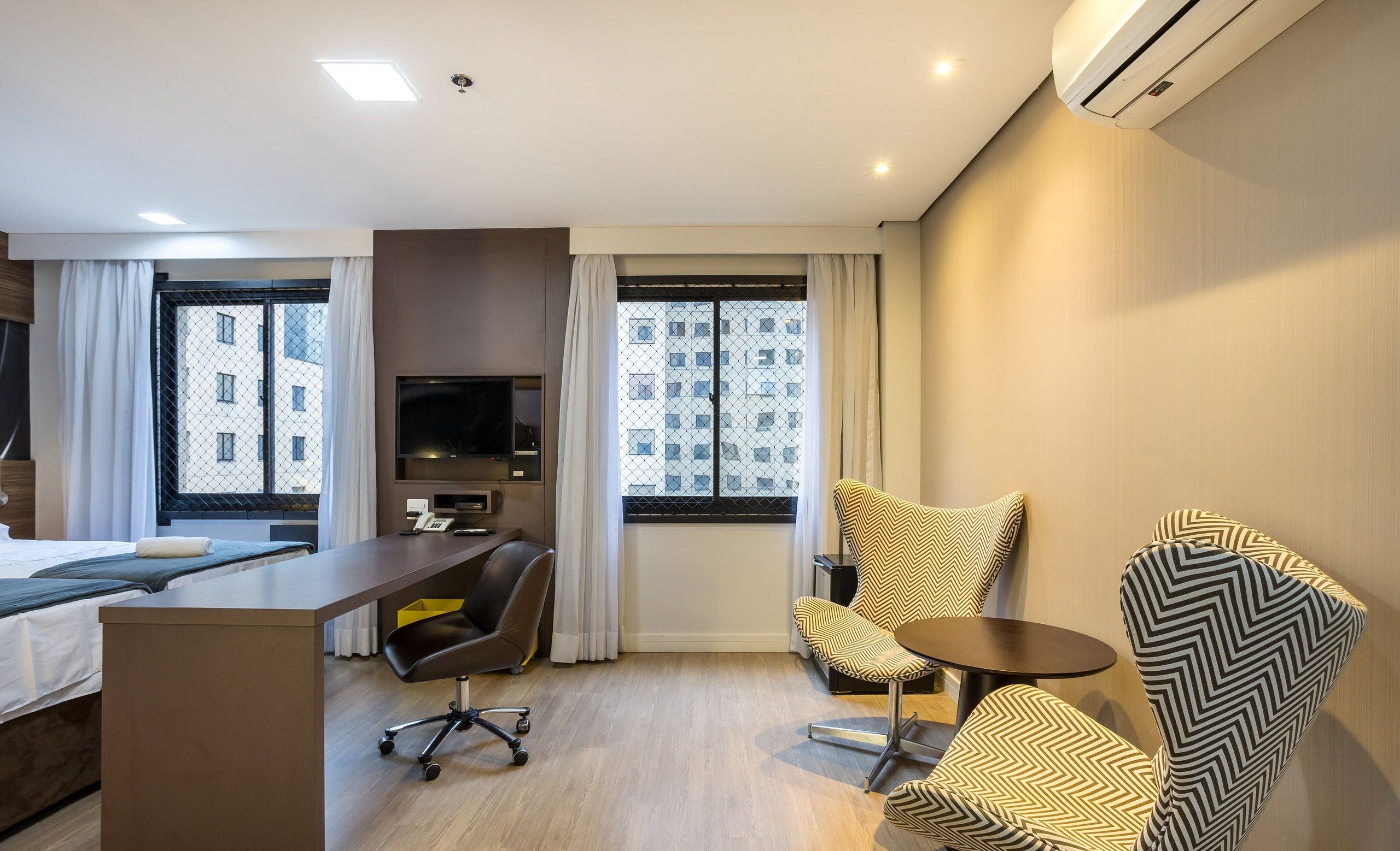 Quarto de hotel moderno com uma cama, escrivaninha e duas cadeiras estampadas.