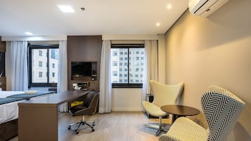 Quarto de hotel moderno com uma cama, escrivaninha e duas cadeiras estampadas.