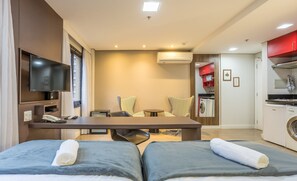 Habitación de hotel con cama, escritorio, televisor, silla, mesa y zona de cocina.