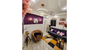 A modern living room with a purple accent wall, a brown armchair, a sofa with colorful cushions, and a patterned rug. - Amour Bandra: A Cozy Affair at Chapel Rd (Mumbai)