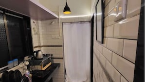 A narrow hallway with a black countertop, a kettle, and a coffee maker. There are two pendant lights, one black and one yellow. The walls are tiled, and there is a white curtain in the background. - Amour Bandra: A Cozy Affair at Chapel Rd (Mumbai)