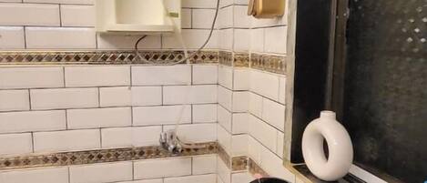 Una cocina con paredes de azulejos blancos, una encimera negra, un lavabo y una ventana con un jarrón blanco decorativo.