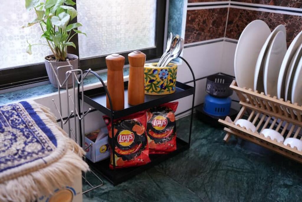 Une cuisine avec une fenêtre, une plante, un étagère à épices, un égouttoir à vaisselle et des paquets de chips Lay's.