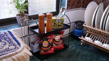 Une cuisine avec une fenêtre, une plante, un étagère à épices, un égouttoir à vaisselle et des paquets de chips Lay's.