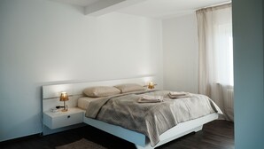 A modern bedroom with a large bed, bedside lamps, and a window with curtains. - Central vacation home, near Legoland and city center, with river view - For families (Günzburg)