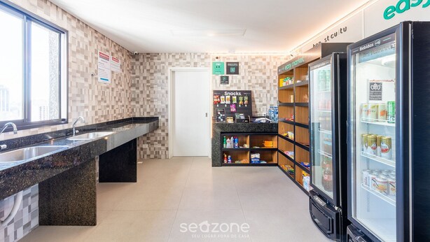 A modern bathroom with a large sink, a mirror, and a toilet. There are shelves with toiletries and a refrigerator with beverages. - Charming Apartment in Curitiba Nlv0506 (Curitiba)