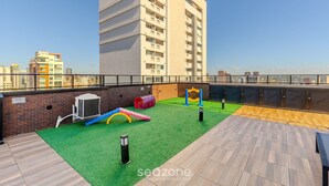 A rooftop with a play area, including a slide and climbing wall, and a view of the city skyline. - Charming Apartment in Curitiba Nlv0506 (Curitiba)