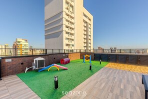 A rooftop with a play area, including a slide and climbing wall, and a view of the city skyline.