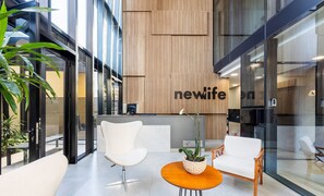 A modern reception area with a 'newlife' sign, two white chairs, a wooden table, and a potted plant.