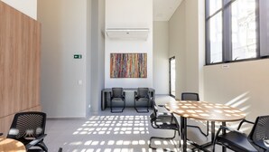 A modern conference room with a round table, two chairs, a colorful abstract painting, and a window with a view of buildings. - Charming Apartment in Curitiba Nlv0506 (Curitiba)