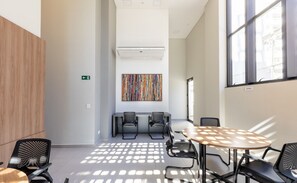 A modern conference room with a round table, two chairs, a colorful abstract painting, and a window with a view of buildings. - Charming Apartment in Curitiba Nlv0506 (Curitiba)