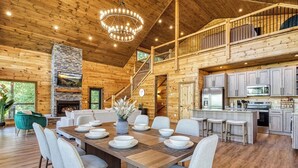 A spacious wooden cabin interior with a dining area, kitchen, and a fireplace.