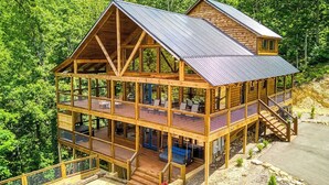 A two-story log cabin with a metal roof, multiple balconies, and a stone foundation.