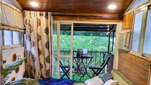 Una habitación acogedora con una cama, una mesita y una silla. Hay una ventana con cortinas y vistas al verdor exterior.