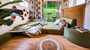 Una habitación acogedora con techo de madera, una cama con almohadas, un sofá verde y una ventana con vistas a la vegetación.