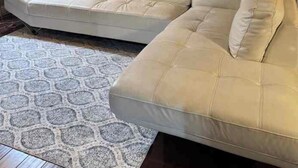 A living room with a white leather sofa, a patterned rug, a painting on the wall, and a window with blinds. - Gated community 2-bedroom,1 bath attached apartment in Manteca (Manteca)