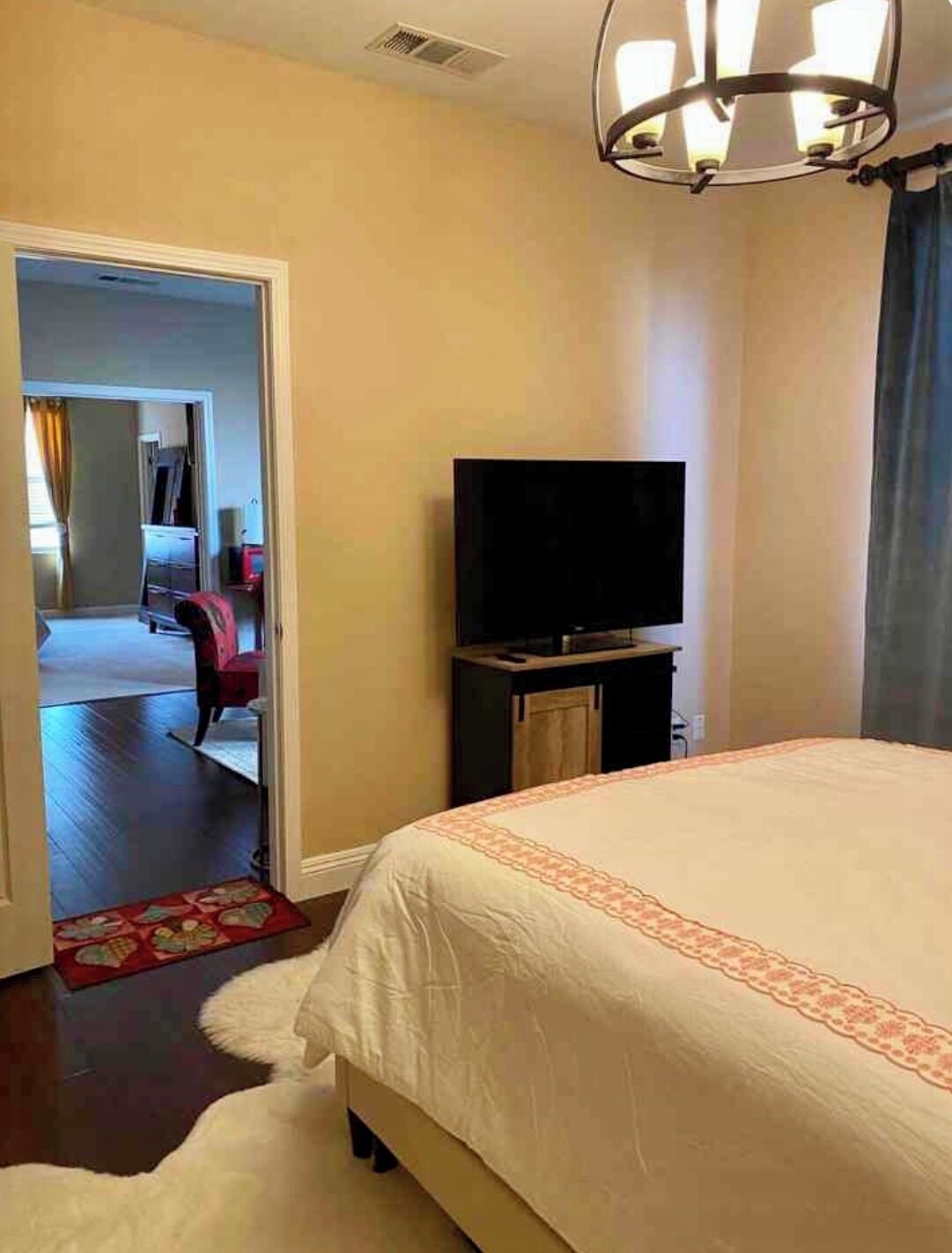 Ein Hotelzimmer mit einem großen Bett, einem Fernseher auf einem Tisch, einer Tür zu einem anderen Raum und einem roten Teppich im Flur.