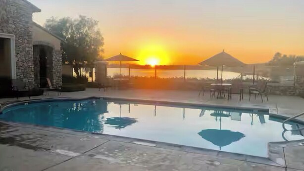 A swimming pool with a sunset in the background, surrounded by lounge chairs and umbrellas. - Gated community 2-bedroom,1 bath attached apartment in Manteca (Manteca)