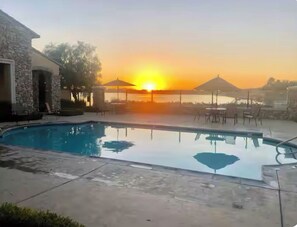 A swimming pool with a sunset in the background, surrounded by lounge chairs and umbrellas. - Gated community 2-bedroom,1 bath attached apartment in Manteca (Manteca)