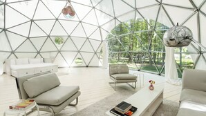 A modern, geometric interior with a white sofa, a coffee table, and a hanging light fixture. - Outlier Inn Large Dome on Farm Upstate Catskills (Woodridge)
