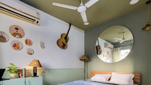 Un dormitorio con cama, ventilador de techo, espejo y adornos en la pared, incluyendo una guitarra y obras de arte circulares.