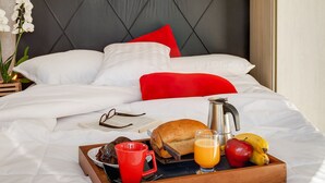 A neatly made bed with white and red pillows, a tray with breakfast items, and a painting of a sunset above the bed. - Studio c/ churrasq 650m da Torre Panorâmica RME047 (Curitiba)